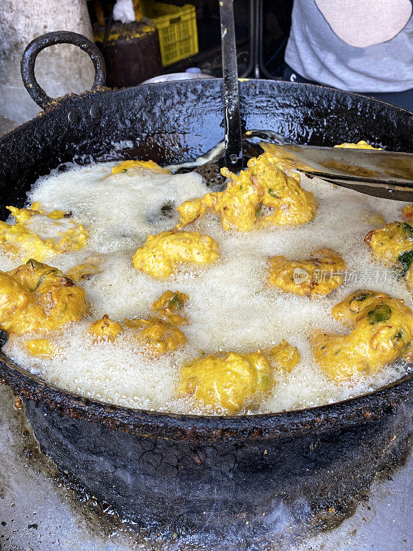 金色的Medu vada(软油条)早餐小吃，户外炉子上的街头小吃，厨师用开槽的勺子转动由Vigna mungo(黑扁豆)制成的美味甜甜圈，煎锅里的油沸腾，前景的焦点上升